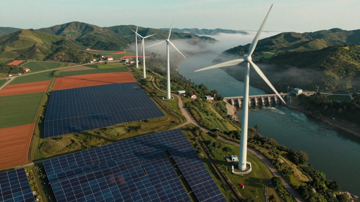 Vista aérea de un valle con huertos solares, aerogeneradores en la cresta y una pequeña presa en el río.