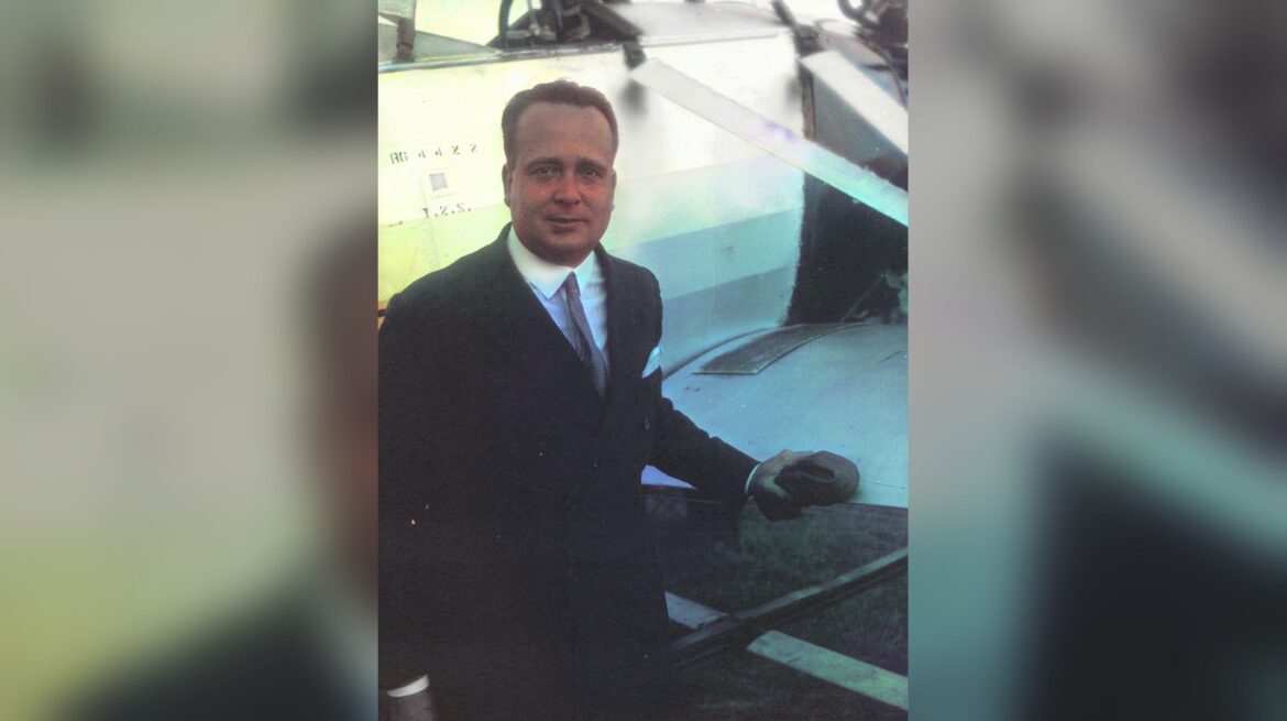 Colourised photo: Juan de la Cierva in a dark suit and tie, standing beside his autogiro at Le Bourget in 1928.