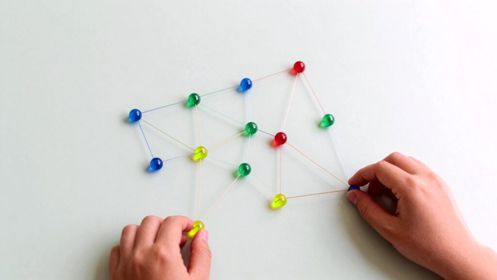 Dos manos colocan cubos luminosos azules, verdes, amarillos y rojos formando una pequeña escalera sobre una mesa verde claro.